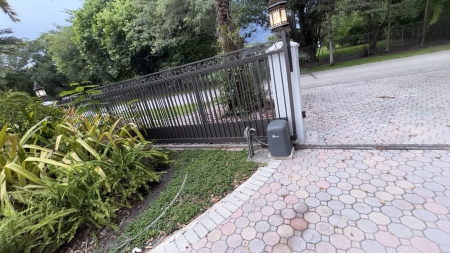 Sliding gate track and operator beside a paver driveway